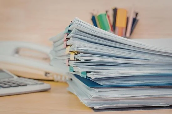 &iacute;r&oacute;asztalon l&eacute;vő pap&iacute;rok egy hivatalban. h&aacute;tt&eacute;rben telefon &eacute;s &iacute;r&oacute;eszk&ouml;z&ouml;k, valamint fontos elint&eacute;znival&oacute;kat tartalmaz&oacute; jegyzetek