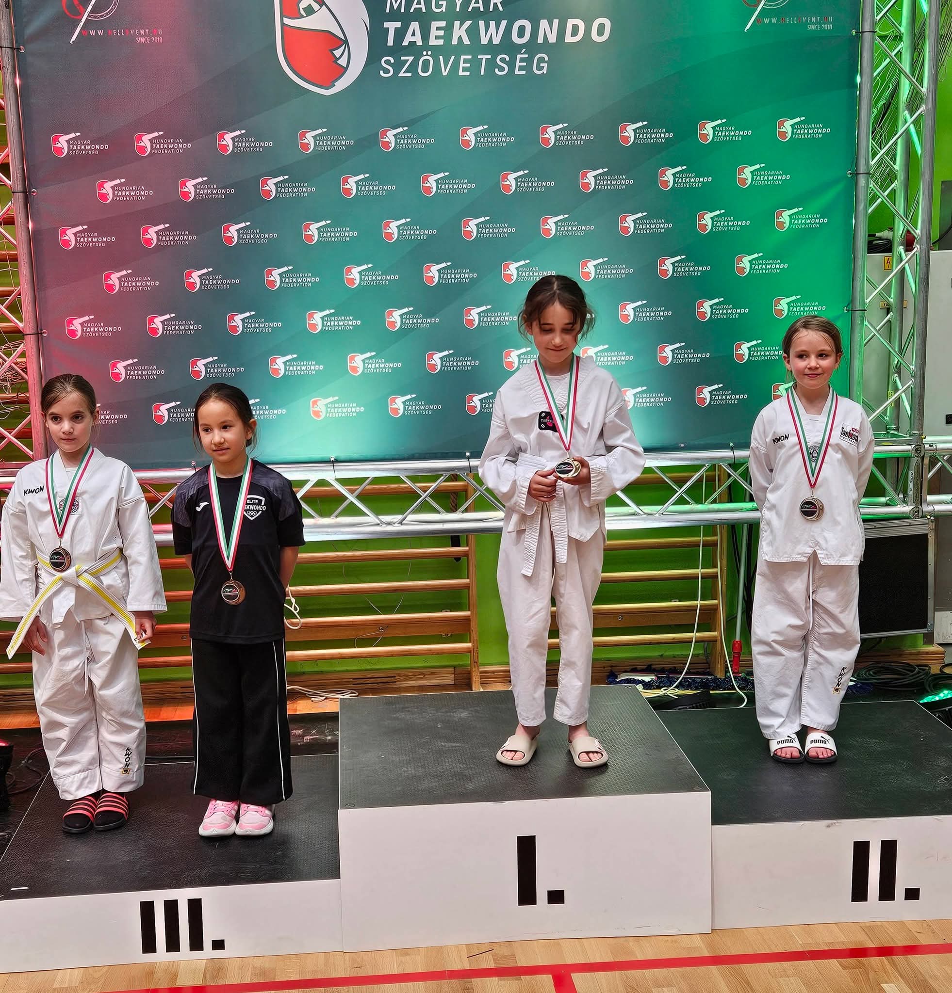 A k&eacute;pen egy taekwondo verseny eredm&eacute;nyhirdet&eacute;se l&aacute;that&oacute;. Gyermek korcsoport, l&aacute;nyok. Első &eacute;s m&aacute;sodik helxyett egy fő, hamradik helyen k&eacute;t fő v&eacute;gzett.